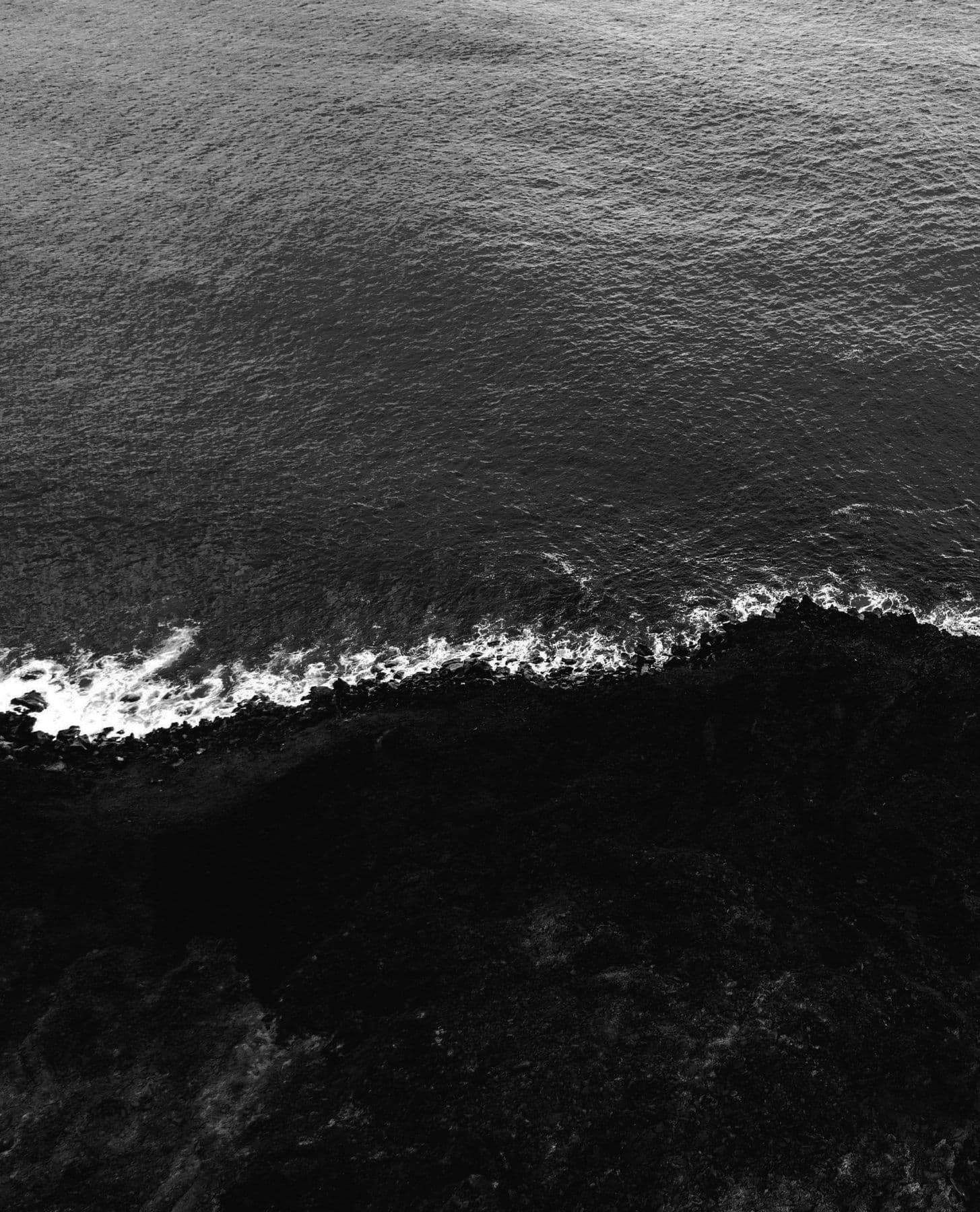 The ocean breaking on a black-sand shore, from above