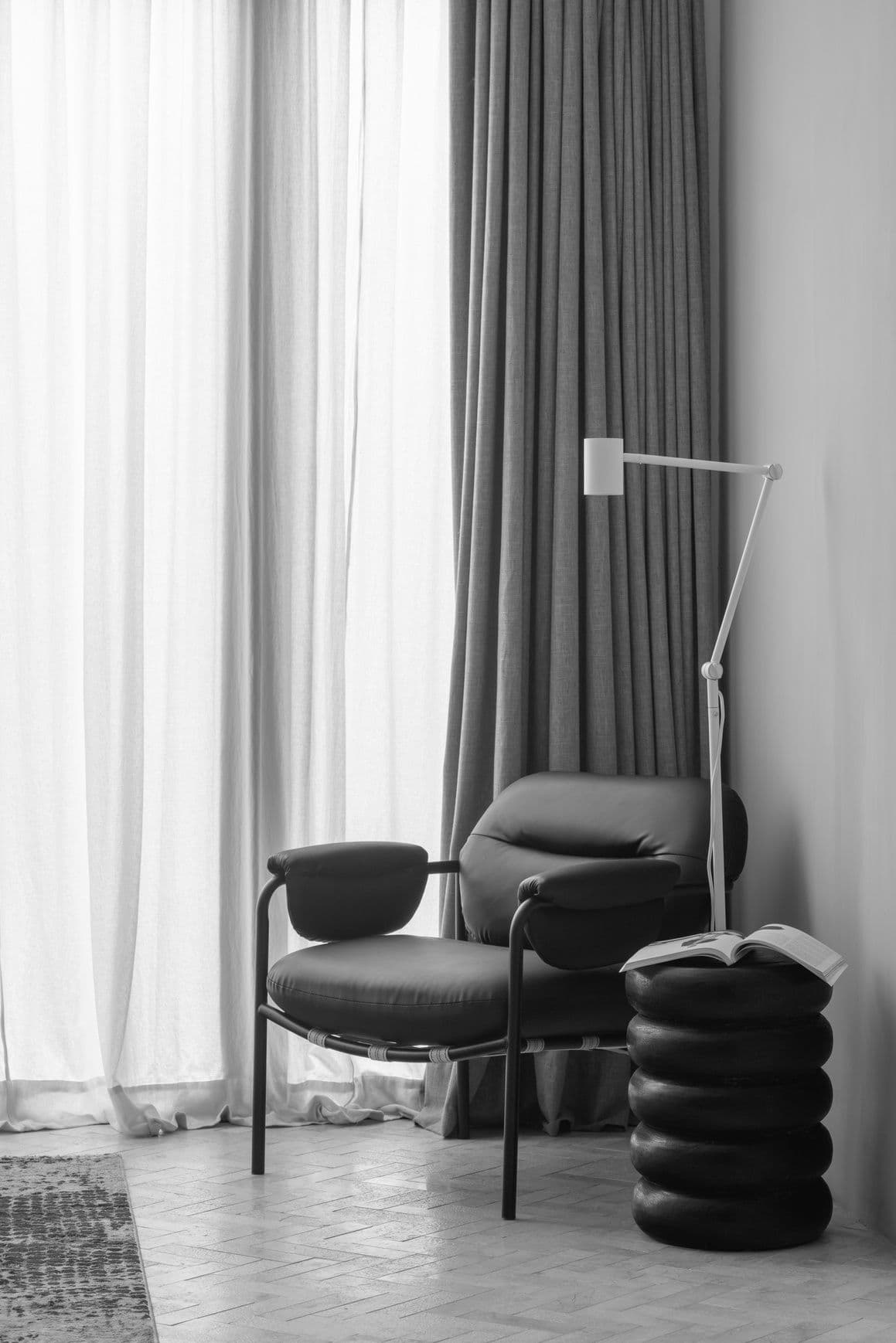 A lounge chair by a curtained window
